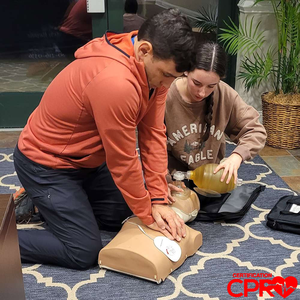 Man and woman practicing CPR on a mannequin during class.